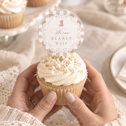 Hands holding a cupcake with a We Can Bearly Wait teddy bear cupcake topper in beige gingham and lace