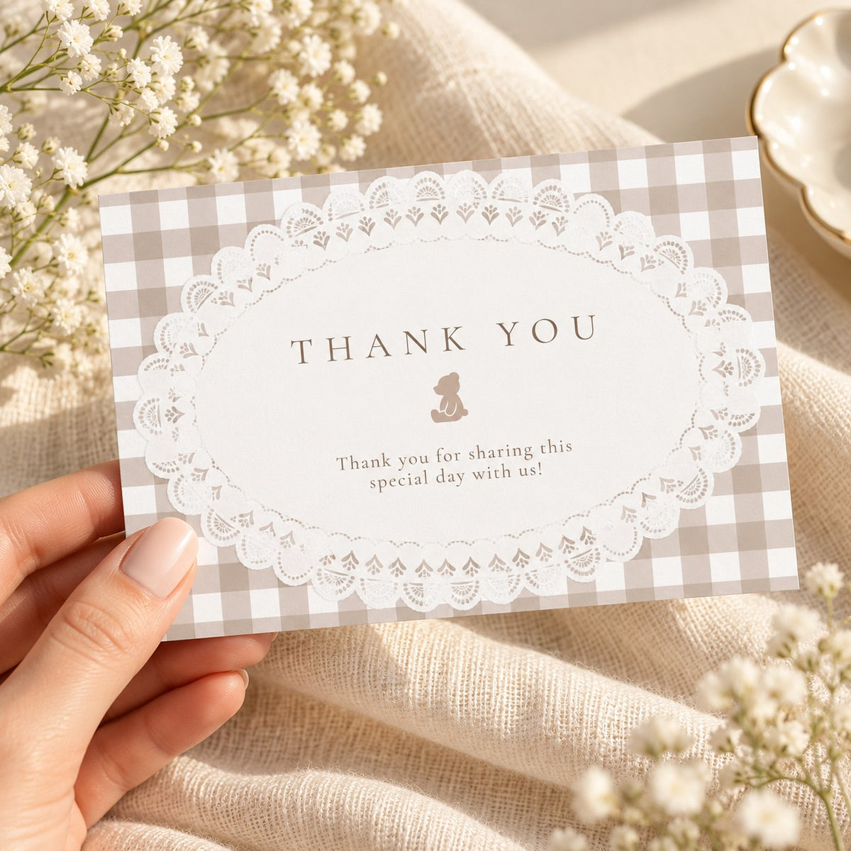 Hand holding a printed teddy bear baby shower thank you card in beige gingham