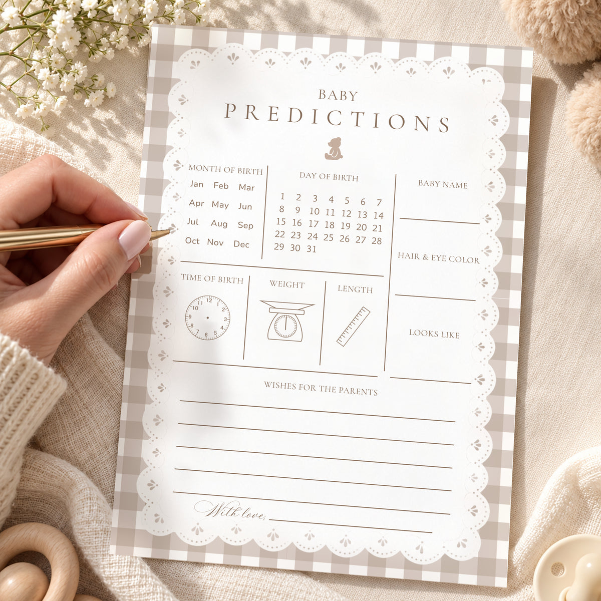 Hand filling in a teddy bear gingham baby predictions card with lace border on a cozy blanket