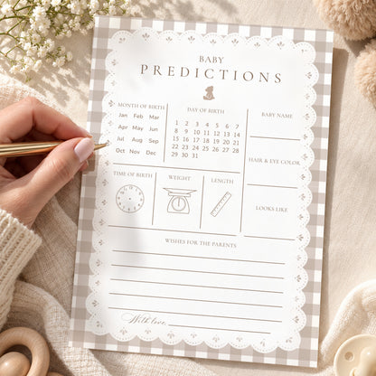 Hand filling in a teddy bear gingham baby predictions card with lace border on a cozy blanket