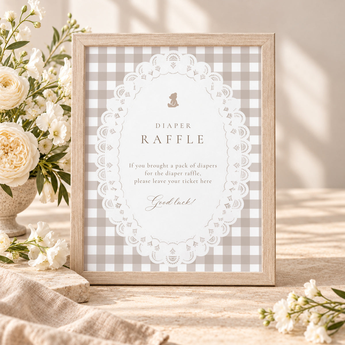 Teddy bear gingham diaper raffle sign in a wooden frame with white flowers at a baby shower